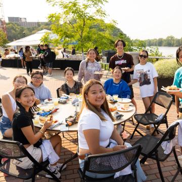 A group of students smile while eating during the Welcome Back Picnic.