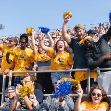 Blugolds throw their hands in the air, holding pom poms, cheering and celebrating the Homecoming football game.
