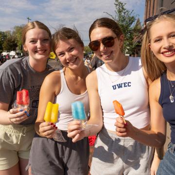 Four Blugolds wearing UWEC attire hold popsicles and smile at the camera.