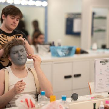 Student playing Frankenstein's monster getting makeup done before show 