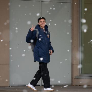 A student shows a peace sign as snow falls in the background.