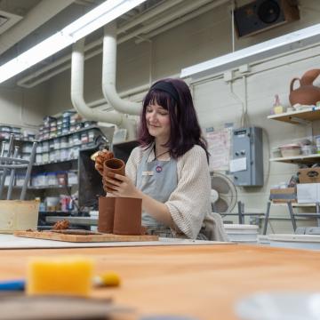 Blugold Greta Wright smiles while working on her pieces of pottery.