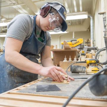 Blugold Renee Ewer concentrates while using sandpaper, surrounded by various tools.