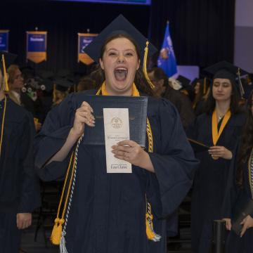 A student laughs gleefully displaying her diploma during Commencement.