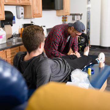 A student tapes another student's foot in a physical therapy space.
