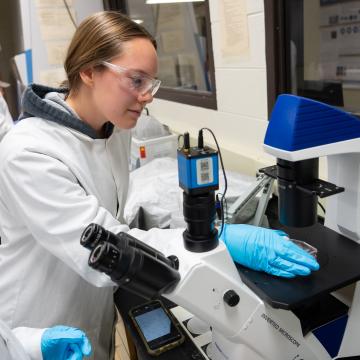 Students dressed in lab coats work with microscopes during a Biomedical Engineering class.
