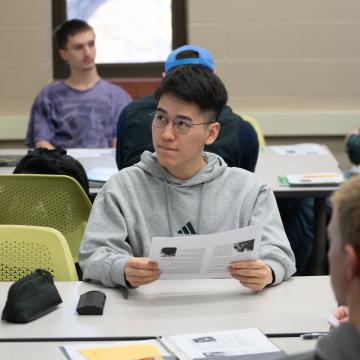A student compares notes next to a smart board in a classroom.