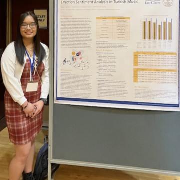 Honors student Nguyen Nguyen stands in front of a poster presentation