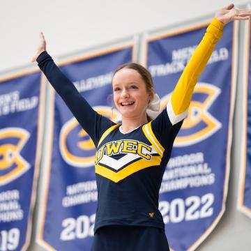 A cheerleader puts her hands in the air against a backdrop of UWEC banners.
