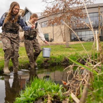 Honors students Hannah Schindler and Lexi Siegmund in camouflage waders