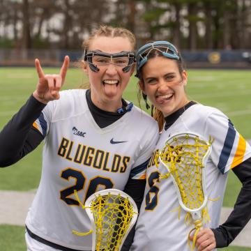 Two lacrosse players pose for a funny photo on the playing field while wearing their uniforms