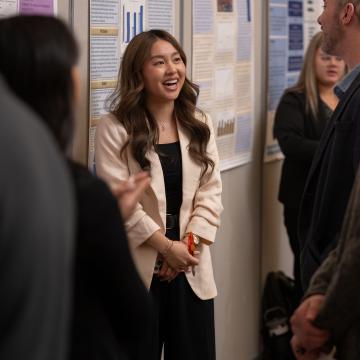 An HCAD student smiles while standing in front of their project poster and speaking with event goers
