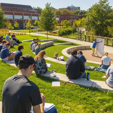 A class sits in the outdoor classroom on campus during a sunny day.