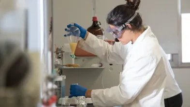 female chemistry student in lab, coat and goggles