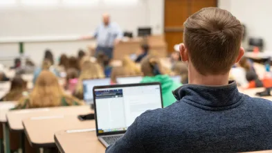 back of male student's head in classroom lecture, laptop open