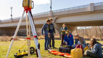 geogrpahy students mapping on the river bank by footbridge