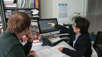 Two people look at a computer screen showing sheet music