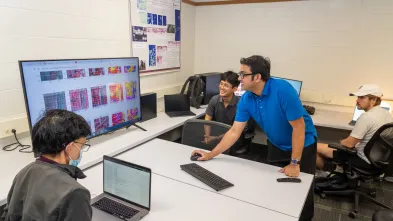 A professor and a student smile while working on a large computer together.