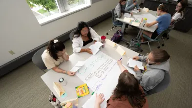 Four students at a table write on a large piece of paper during a group activity in class.
