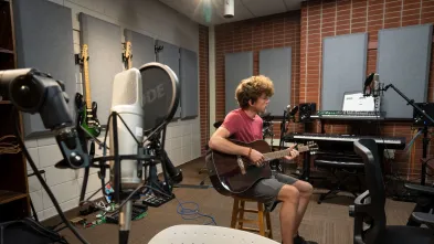 Student plays the guitar in UWEC's audio room 