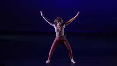 Dancer barefoot on stage extends arms and legs into an "x" formation