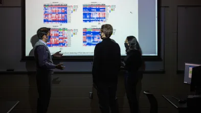 Computer science students standing in front of a projected image discussing