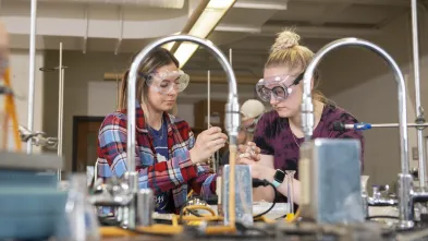 Students wearing goggles conduct an experiment in a chemistry lab.