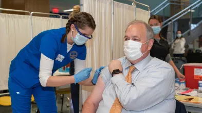 Chancellor Schmidt receiving a vaccination from a nursing student