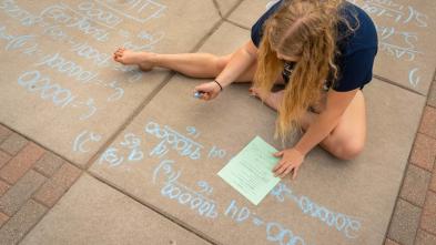 student outside doing math problem on sidewalk for class