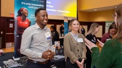 two career fair visitors speaking with students, one is alumnus