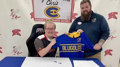 Two people pose for a photo at a table with the UWEC Esports logo.