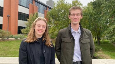 Two students in front of Davies, jackets on, standing on the bridge