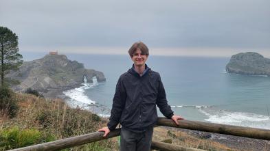 Calvin Lutzke stands in front of a railing overlooking a sea.