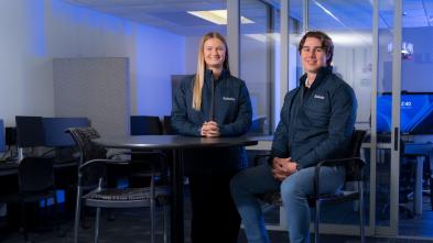 Two young alumni staff members of Solutia Consulting in branded coats 