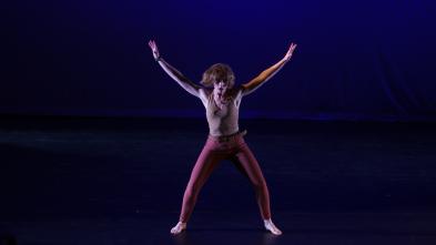 Dancer barefoot on stage extends arms and legs into an "x" formation