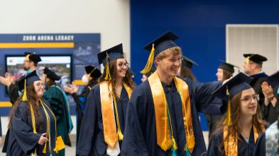 Graduates wearing graduation caps and gowns walk in a line into the ceremony on commencement day