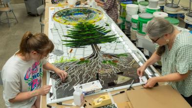 Art student and faculty making stained glass on a long table