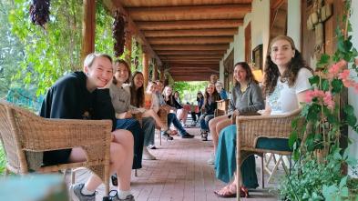 New Mexico immersion students sit across from each other, down a long, covered porch, with plants and greenery around