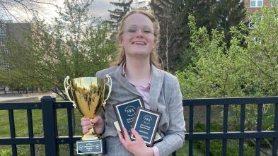 Austyn Clemen smiling and holding an embarrassment of Forensics competition riches