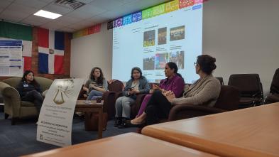 A panel of speakers sit in front of a projector screen at an event.