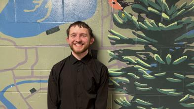 Jayson Coleman smiling in front of a mural in the Haas Fine Arts Building