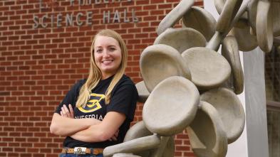 Female student leaning on sculpture outside science building