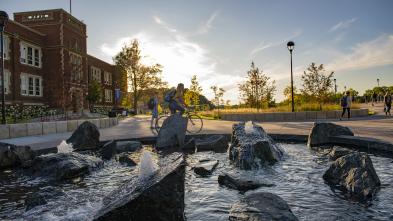 Students walk and bike next to the Stowe Fountain during a sunset on campus