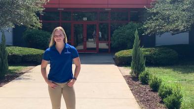 female student standing in front of commercial building, blue shirt says Rust-Oleum