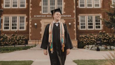 Jordan Blue smiling  in cap and gown in front of Schofield Hall, summer or fall sunset hour
