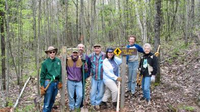 Group gathers for a photo in the woods by sign that reads "Ice Age Trail."