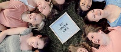 Students laying in a circle around a Go Greek Life sign in the middle