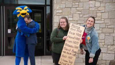 Students holding a sign and student hugging mascot