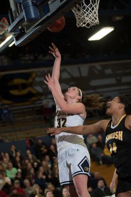 Blugold women's basketball player in white uniform shooting a layup under the hoop