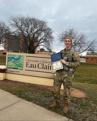 student in army fatigues stands in front of UWEC sign